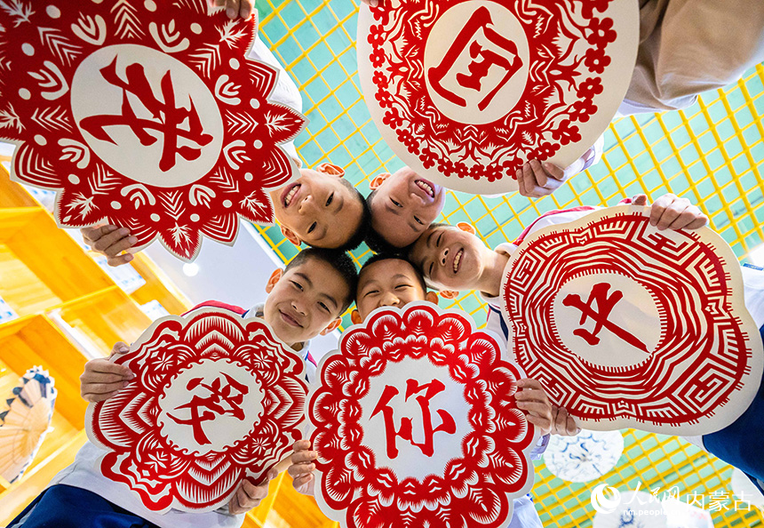 呼和浩特市玉泉區(qū)恒昌店巷小學(xué)五里營校區(qū)的學(xué)生在展示創(chuàng)作的“我愛你中國”團(tuán)花剪紙作品。丁根厚攝